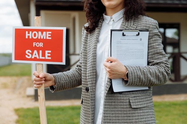 person holding a home for sale sign and contract