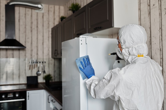 Person in a white hazmat suit cleaning a fridge