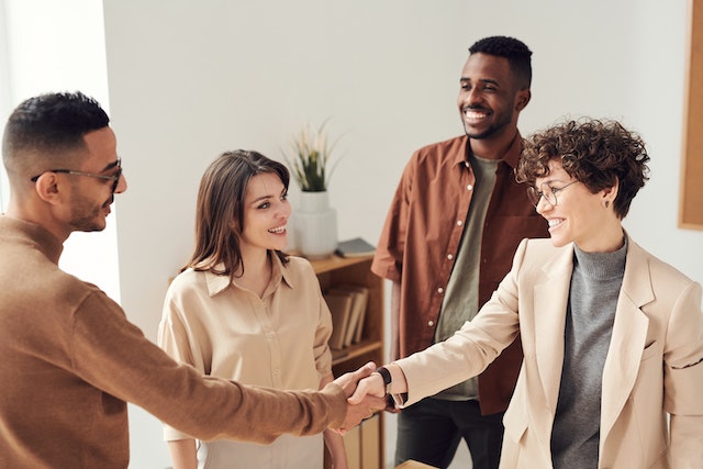 four people standing in a room as two people shake hands