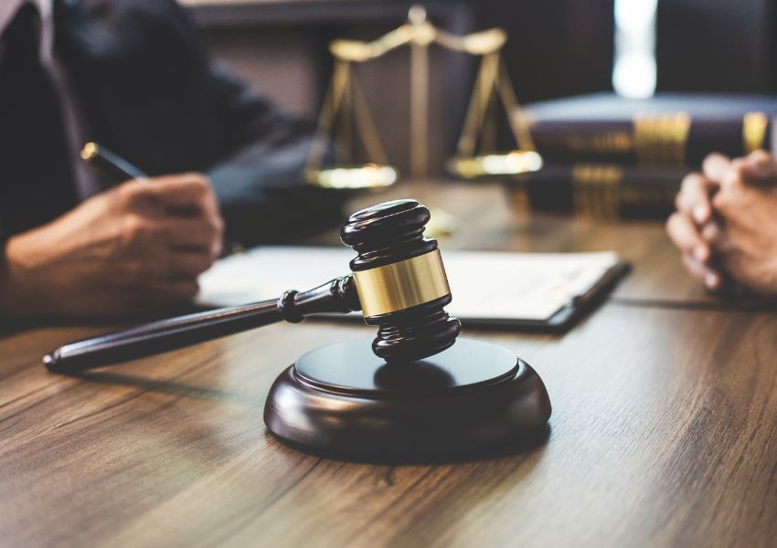 judges gavel on their desks along with a legal scale as they sign a document in the background