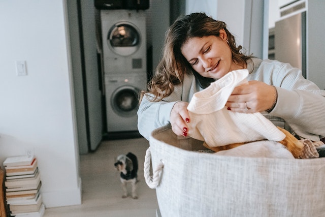 person doing laundry with washer and dryer and a little dog behind them