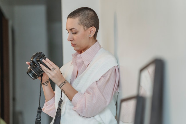 person in a pink shirt and white sweater looking at a photo they just took on their camera