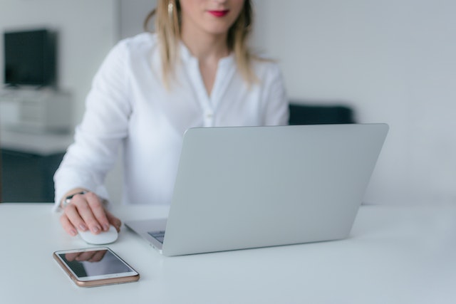 person in a white shirt working on their laptop with their phone next to them