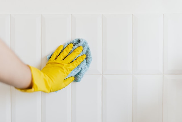 person wiping down white tiles with a blue cloth