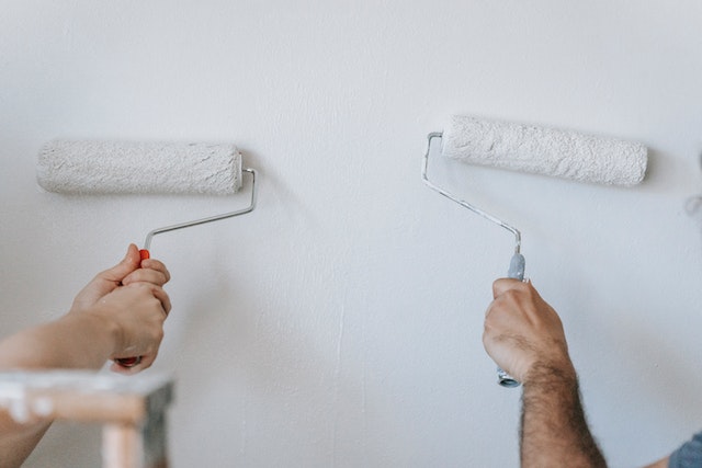 two hands each holding paint rollers with white paint on them