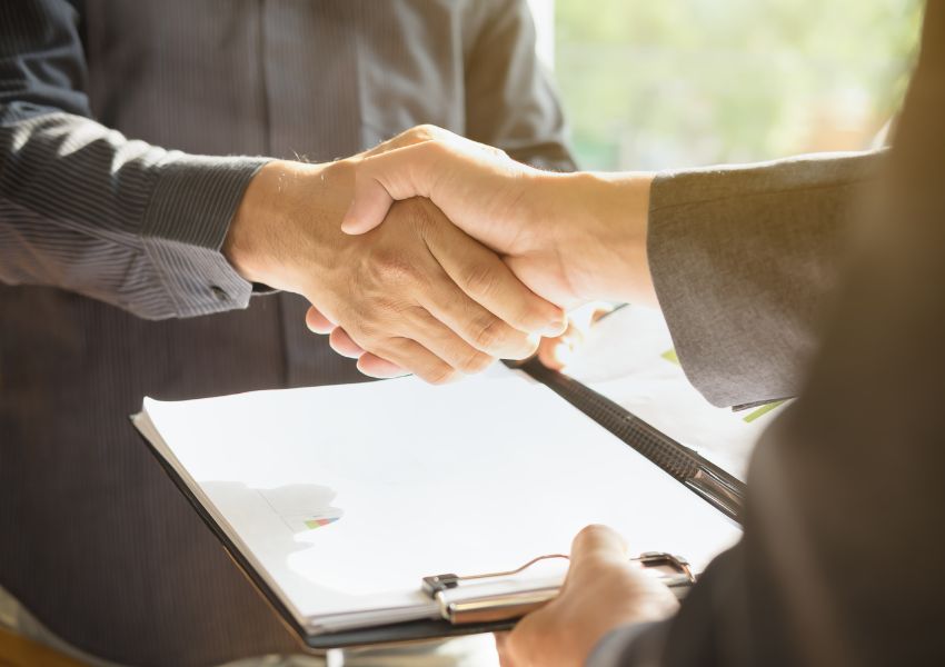 two people shaking hands across a document on a clipboard