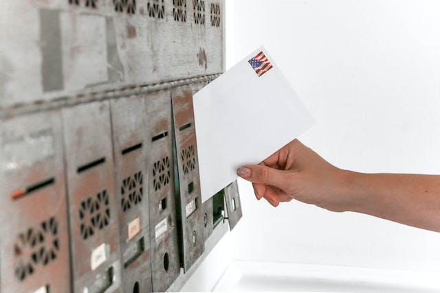 white letter being placed in a community mailbox